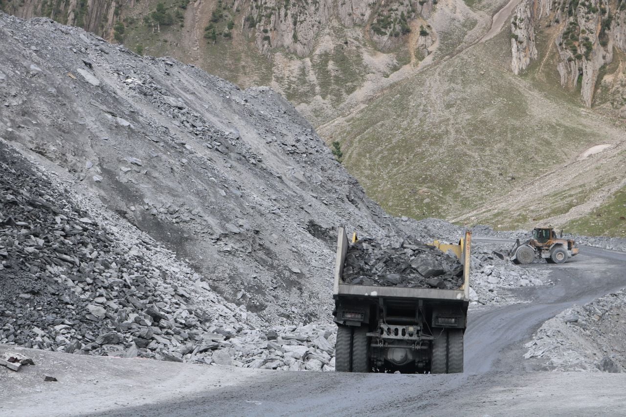 hero-img-02 A quarry with trucks and machinery operating amidst rugged mountain terrain.